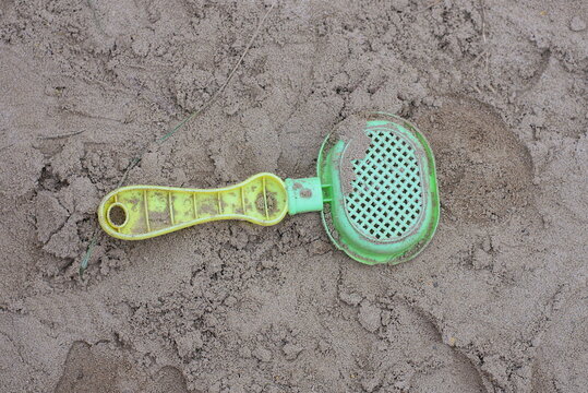 a one small green yellow dirty plastic baby scoop is lying on gray sand