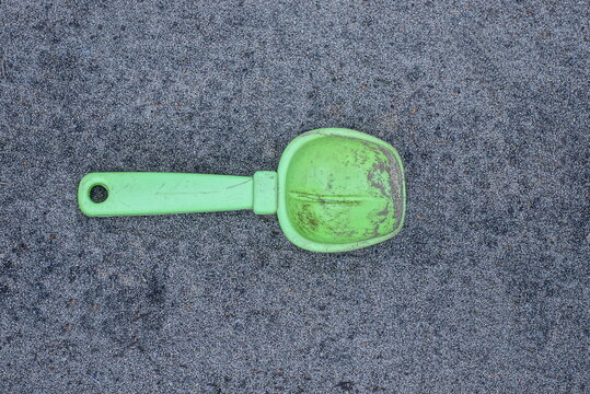 a one small green dirty plastic baby scoop is lying on gray sand