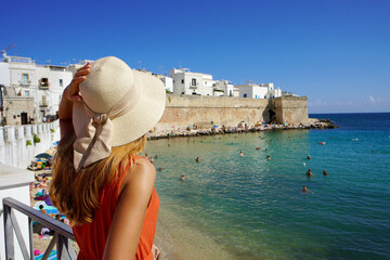 Rear view of young woman with hat and dress enjoying seascape in Monopoli town, Bari, Italy