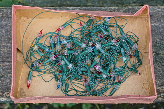 a skein of an old green electric Christmas garland with small colored light bulbs lies in a brown paper box on a gray table