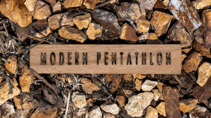 modern pentathlon. Written on wooden surface. Wooden frame on pieces of stone. Sports and adventure
