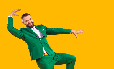 Funny man in a green suit dancing in the studio. Portrait of a happy, cheerful guy wearing a green suit dancing isolated on a bright yellow colour background. Party, fashion, having fun concept