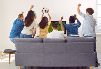 Back view of sport fans men and women friend sitting on couch watching soccer football match on TV...