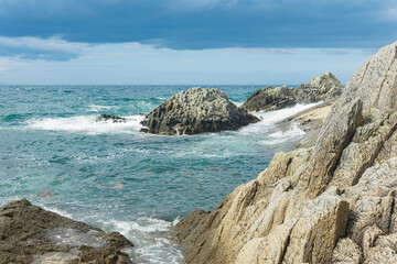 rocky seashore formed by columnar basalt against the backdrop of a stormy sea, coastal landscape of the Kuril Islands