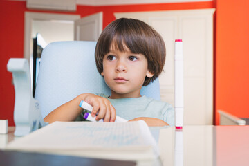 Smart kid with a notebook studying online at his colorful room remotly during pandemic