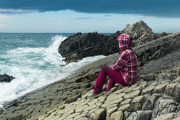 traveler sits on the shore of a stormy sea, on a natural pavement made of columnar granite