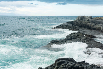 rocky seashore formed by columnar basalt against the backdrop of a stormy sea, coastal landscape of the Kuril Islands