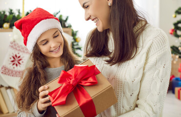 Fototapeta na wymiar Smiling loving mom congratulate excited little teen daughter give present on New Year eve. Happy caring mother greeting small girl child with Christmas with gift. Winter holiday concept.