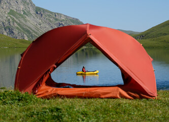Tent on Mountain Lake with Woman Paddling on Packraft on Background.