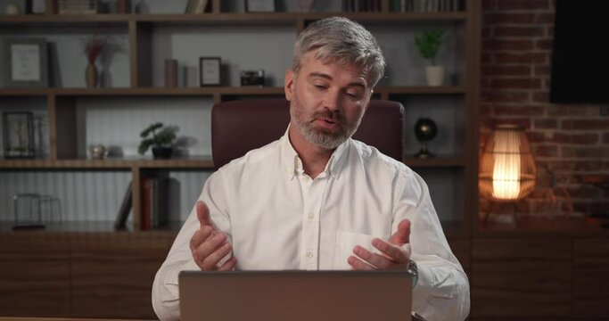 Successful man talking over laptop webcam in virtual chat sitting at workplace