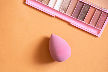 Pink sponge and multi-colored shadows lie on a colored background, beauty and makeup, cosmetics