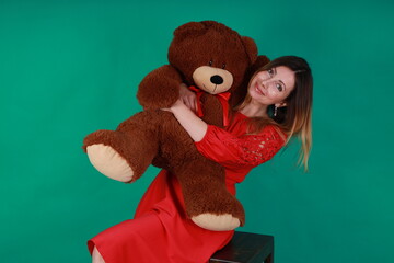 Beautiful woman in red dress hugging a teddy bear