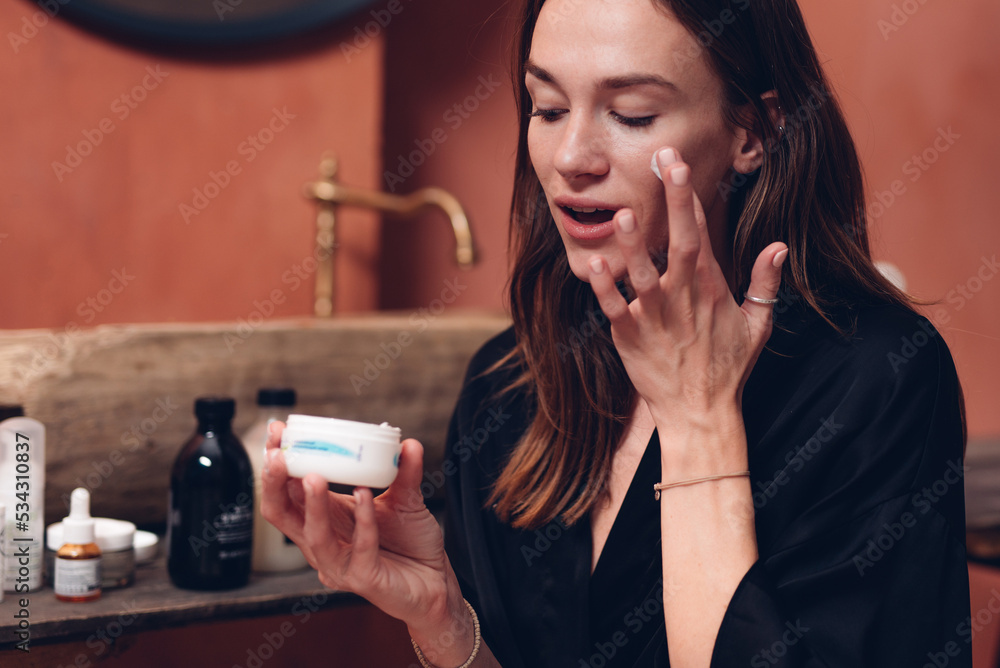 Wall mural Young woman applying cream on her face