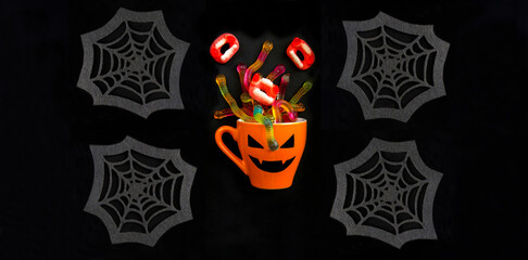 Orange cup with candy for Halloween and decorative spider web  on the black background. Halloween background. Closeup.