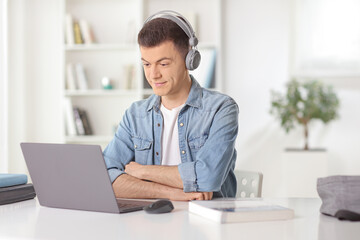 Young man sitting in front of a laptop at home and listening a tutorial