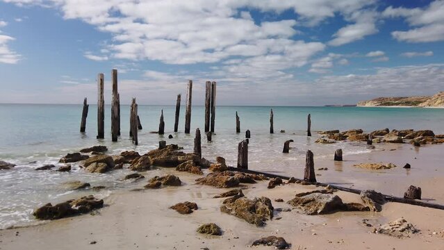 Right to left panning motion of the ruins and Pylons that Remain of the 1860s jetty on the beach at Port Willunga, south Australia, Australia