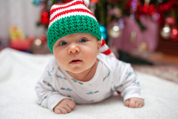 Adorable little baby boy in knitted red green hat on white blanket