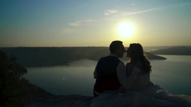 Silhouette of asian couple in love sitting on the top of the hill peak at sunset