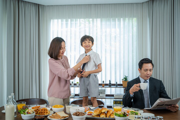 Parents helping son in uniform to get ready to leave home for school.