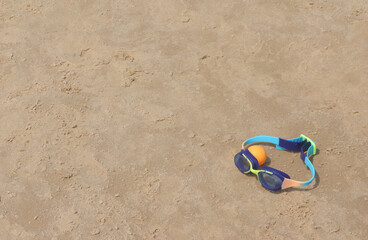 Swimming children's goggles lie on the sand and next to a plastic ball