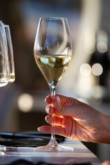 A right hand holds a crystal glass with white wine