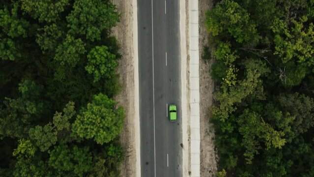 Cinematic aerial top down view of the green car on the road between green forest. Drone slow motion shot of the road in the forest.