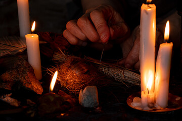 Voodoo doll in the hands of an old witch with a needle in her heart in the dark against the...