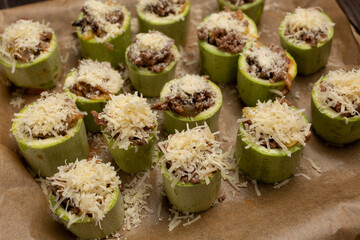 Young zucchini cut into portions, stuffed with minced meat, sprinkled with hard cheese, prepared for baking
