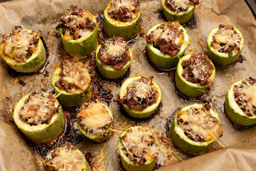 Young zucchini are cut into portions, stuffed with minced meat, sprinkled with hard cheese, baked in the oven