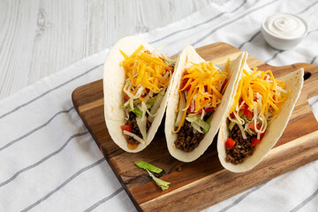 Homemade American Beef Tacos with lettuce, tomato and cheese on a wooden board, side view. Copy space.