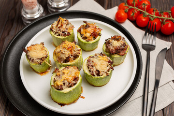 Young zucchini cut into portions, stuffed with minced meat, sprinkled with hard cheese, baked in the oven, laid out on a plate