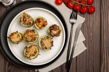 Young zucchini cut into portions, stuffed with minced meat, sprinkled with hard cheese, baked in the oven, laid out on a plate, open space, flat lay
