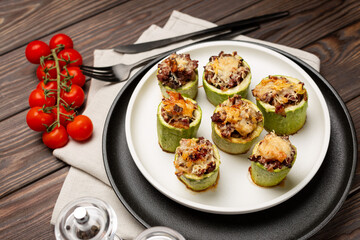 Young zucchini cut into portions, stuffed with minced meat, sprinkled with hard cheese, baked in the oven, laid out on a plate, open space