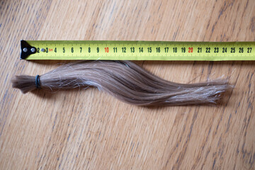 Long cut off natural blond ponytail hair tied together next to tape measure. Hair donation.