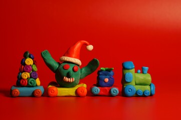 A toy train with a Christmas tree gift and a virus figurine in a festive hat. Christmas toys. A festive event. New Year and Christmas. Red background.