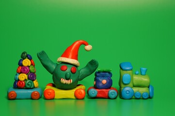 Obraz premium A toy train with a Christmas tree, a gift and a figure of a virus in a festive hat. Christmas toys. A festive event. New Year and Christmas. Green background.