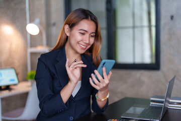 Obraz premium Beautiful Asian businesswoman using a smartphone to contact customers reply to chat Transact on social media applications in the office with a smiling face.