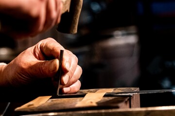 Closeup of a metalworker with a hammer and nail punching an inscription into a piece of steel