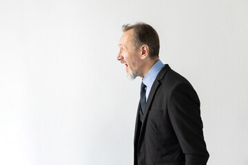 Portrait of angry mature businessman looking away and shouting. Side view of senior Caucasian manager wearing three piece suit crying with irritation against white background. Angry boss concept