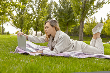 The woman is lying down using a laptop in the park.