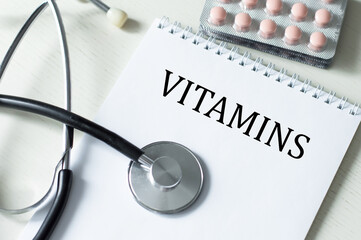 text vitamins text on a notebook on the table next to it is a stethoscope and tablets