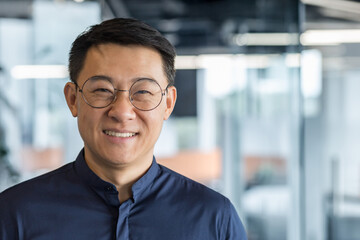 Close up photo portrait of successful young Asian investor, man in glasses smiling and looking at...