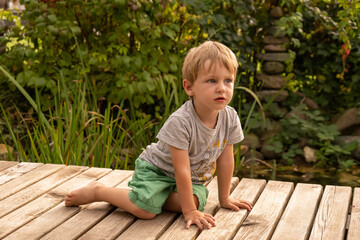 Little boy in green shorts sitting on a deck in the backyard