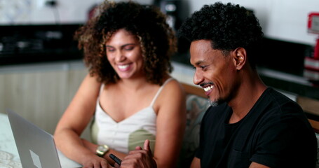 Candid black couple laughing and smiling together at home kitchen table
