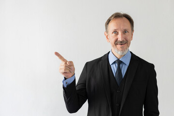 Portrait of smiling mature businessman showing something. Senior Caucasian sales manager wearing three piece suit looking at camera and pointing with finger. Presentation concept