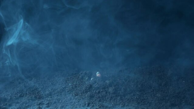 The zombie's hand breaks through the black earth in the fumes of smoke.