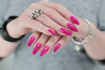 Woman hand with long nails manicure and pink fuchsia bottle with nail polish