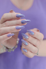 Female hand with long nails and a bottle of light lilac purple color nail polish
