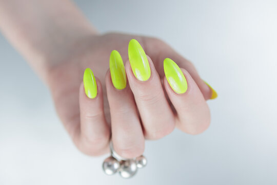 Female Hand With Long Nails And A Bottle Of Bright Yellow Green Neon Nail Polish