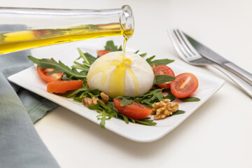 Fresh traditional buratta cheese with arugula leaves and cherry tomatoes is drizzled with olive oil before serving. Italian cheeses